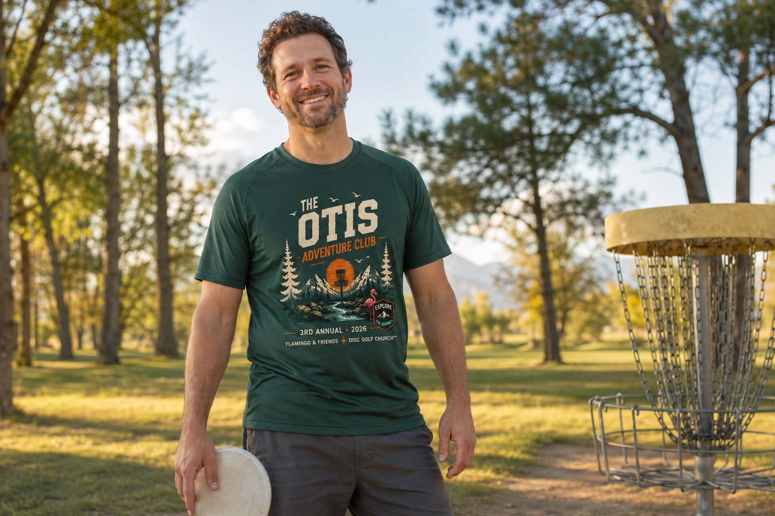 Disc golfer wearing The Otis Adventure Club short-sleeve performance T-shirt beside a basket